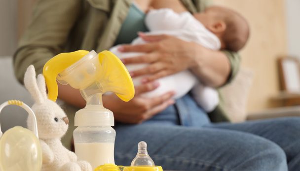 Breast pump with baby pacifier and toy on table in room, closeup
